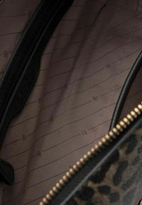 Intérieur d'un sac à main à motifs léopard, featuring un doublure beige lisse avec de subtiles rayures et une poche zippée noire pour le rangement.