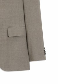 Manche de veste de costume beige sur mesure avec poche à rabat, avec trois boutons foncés au poignet, mettant en valeur la texture du tissu et les détails de couture.
