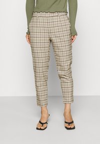 Rutiga byxor i beige och bruna toner, med en avslappnad passform, uppvikta anklar och ett midjeband med volangdetaljer. Matchas med svarta flip-flops.