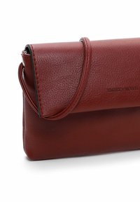 Red leather clutch bag with a textured surface, flap closure, detachable strap, and embossed branding on the side.