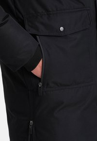 Giacca nera isolata con tasca con zip e tasca con pattina. Caratterizzata da polsini a coste e tessuto morbido. Design durevole e funzionale.