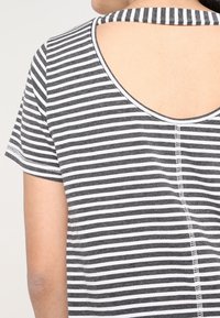 Top de manga corta a rayas en gris y blanco con escote en la espalda y detalles de costura visibles. Tejido suave y liviano con un diseño casual.