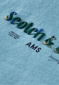 Sudadera azul claro con logotipo bordado texturizado y multicolor "Scotch &" y "AMS", además de pequeños detalles impresos cerca del dobladillo.