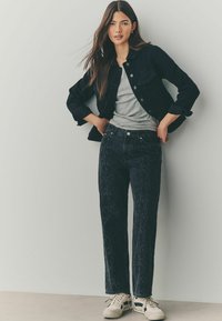 Mustmustest denim jakk ja hall T-särk, millele on kombineeritud tumedad mustrilised teksad ja valged tossud, näidates lõdva istuvuse ja kaasaegset disaini.