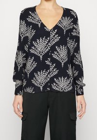 Blouse marine avec un col en V et des manches longues. Présente un motif de feuilles botaniques blanches et une fermeture à boutons à l'avant. Fabriquée en tissu léger.