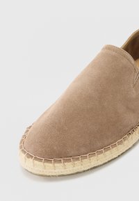 Barna velúr slip-on cipő kerek orral és juta talppal. A talp peremén látható varrás díszíti. Simasága különleges tapintást kölcsönöz.