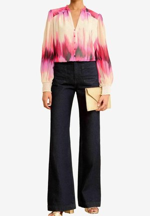 Mujer con blusa de degradado en tonos rosa, rojo y blanco con mangas abullonadas, pantalones anchos de cintura alta oscuros, bolso de mano beige y sandalias doradas.