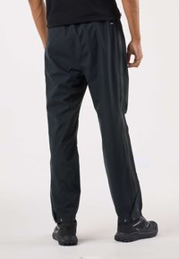 Svarta, lätta, vattentäta byxor med avslappnad passform, utrustade med sidslidingar och resår i midjan för komfort. Kombinerade med svarta skor.