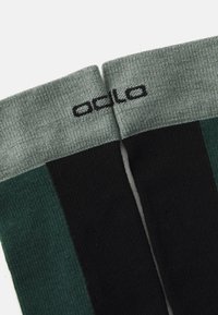 Calcetas hasta la rodilla con un tejido texturizado, que presenta rayas en verde oscuro, negro y gris claro. Logo impreso en el puño gris en negro.