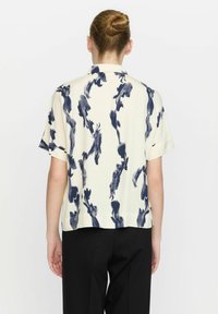 Kurzärmlige Bluse in Creme mit navyfarbenem, abstrahierter Pinselstrich-Muster. Mit Kragen und lockerer Passform. Glatte Textur.