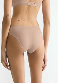 Beige nahtlose Unterwäsche mit glatter Textur, mittelhohem Sitz und dezentem Branding am Bund. Verfügt über einen klassischen Schnitt und ein minimalistisches Design.