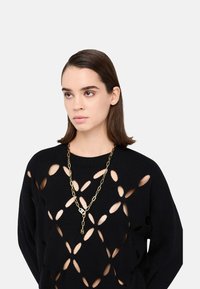 Maglione nero a maglia con grandi motivi traforati, abbinato a una collana a catena dorata con maglie e un ciondolo decorativo.