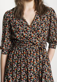 Robe noire à col en V, ornée d'un motif floral multicolore. Manches longues avec poignets froncés et taille marquée, jupe fluide.