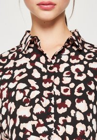 Camicia nera con bottoni, decorata con una stampa leopardata in tonalità di rosa e bordeaux. Presenta un colletto classico e una texture di tessuto liscia.