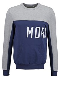 Sweat-shirt col rond avec le haut et les manches gris, poitrine et poche bleu marine, avec de grandes lettres blanches formant "MORA" à l'avant.