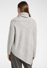 Poncho lavorato a maglia grigio chiaro con un colletto alto, caratterizzato da un motivo a treccia testurizzato e un orlo diagonale. Include dettagli con bottoni sul colletto.