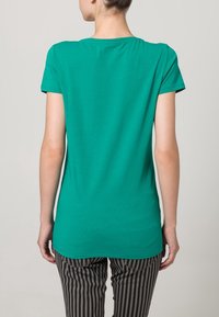 Camiseta verde de manga corta con cuello redondo, que presenta una textura suave y un ajuste relajado, combinada con pantalones a rayas para un contraste.