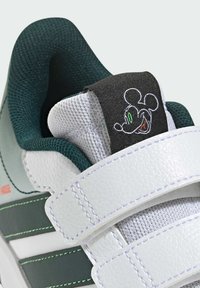 Biele tenisky s prízvukmi v zelenej a sivej farbe. Majú topánky z textúrovanej kože, sieťovanú jazyk a čierny remienok s vyšitým dizajnom Mickey Mouse.