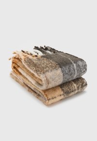 Couverture en laine à carreaux dans des tons de beige, marron et gris, avec des bords frangés et une finition douce et texturée. Repliée soigneusement.