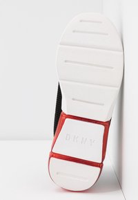 Černá teniska s texturovaným síťovaným svrškem, bílou gumovou podrážkou a červeným akcentem na patě, s vyrytým logem "DKNY".