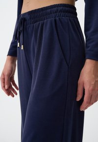 Marineblaue, lässig geschnittene Hose mit gerafftem, elastischem Bund und Kordelzug, vorn mit Falten und glatter Stoffstruktur.
