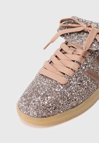 Zapatilla cubierta de purpurina en oro rosa con suela de goma marrón y cordones a juego. Cuenta con una lengüeta acolchada y parte superior texturizada.