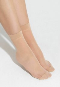 Calze alla caviglia beige con una texture liscia, fascia superiore elastica e logo “JOOP!” stampato in un colore chiaro. Inquadratura ravvicinata dei piedi.