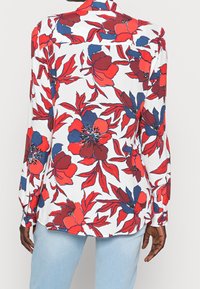 Long-sleeve shirt in white fabric featuring a bold floral pattern in red and navy, with cuffs and a standard collar.