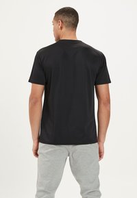 Schwarzes Kurzarm-T-Shirt aus glattem Stoff, mit Rundhalsausschnitt und lockerer Passform, kombiniert mit grauen Jogginghosen.
