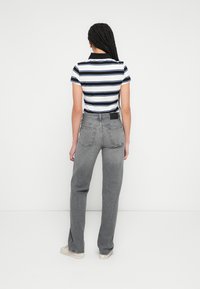 Vertikaalsete triipudega lühikeste varrukatega polo, mille värvid on tumesinine ja valge, sobitatud hallide kõrge vöökohaga sirgete teksadega. Klassikalise krae ja kahe tagataskuga.