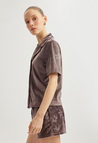 Harmaa velour-kaksiosainen asu, joka sisältää lyhythihaisen kauluspuseron ja siihen sopivat shortsit, molemmissa on kohokuvioidut tähtikuviot. Pehmeä rakenne.
