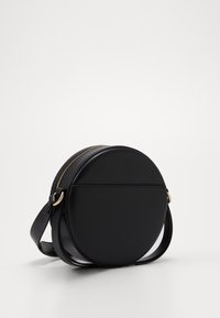 Rund sort læder crossbody taske med guld lynlås, flad profil, justerbar rem og glat tekstur. Ingen synlige logoer eller mønstre.