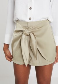 Pantaloni beige realizzati in un tessuto morbido, con un dettaglio di nodo frontale, una silhouette pulita e sartoriale e delle fessure laterali discrete.