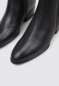 Botas negras hasta el tobillo hechas de cuero texturizado con punta afilada y un tacón bajo. Cierre lateral para ponerlas y quitarlas fácilmente.