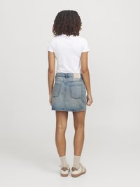 Jeanskjol med ett klipp vid mitten av låret, ljusblå tvätt, två bakfickor, och en vit t-shirt. Skorna inkluderar ljusa sneakers och beige strumpor.