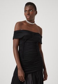 Juoda off-shoulder suknelė, pagaminta iš susiraukšlėjusios medžiagos, turinti prigludusią siluetą ir laisvą sijoną. Pabrėžta kristalo chokeriu.