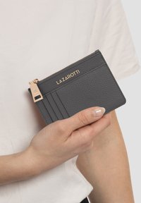 Tarjetero de cuero gris con herrajes en tono dorado, que cuenta con ranuras para tarjetas en un lado y un compartimento con cremallera. Nombre de la marca "LAZAROTTI" grabado.