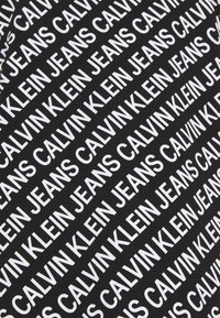 Svart tyg med ett upprepat diagonalt mönster av "CALVIN KLEIN JEANS" i fet vit text. Texturen är jämn och slät.
