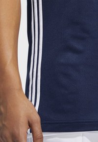 Maritim træningsskjorte med mesh-struktur, der har hvide lodrette striber på siderne og en rund halsudskæring. En hånd viser greb om stoffet.