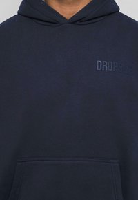 Marineblå hoodie lavet af blødt stof, med en frontlomme og præget "DROPSIZE" logo på venstre bryst. Regular fit design.