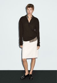 Brown cable-knit sweater, gray collared shirt underneath, white pencil skirt, and black loafers; model standing against a light background.