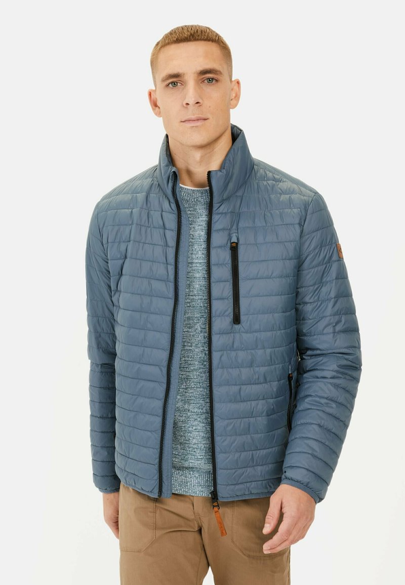 Gevoerde blauwe jas met een staande kraag, horizontaal gestikt ontwerp, frontale ritssluiting en een ritsvak op de borst. Zacht, lichtgewicht materiaal.