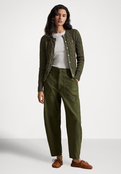 Πράσινη ζακέτα πλεκτή με μοτίβο καλώδιο πάνω από λευκή κοντομάνικη μπλούζα, συνδυασμένη με χαλαρά χακί παντελόνια και παπούτσια σε στυλ μοκασίνι καφέ.