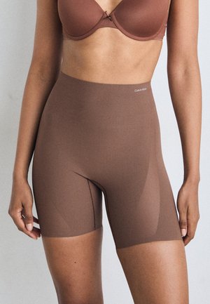 Brown seamless shapewear shorts with a smooth texture, mid-thigh length, and Calvin Klein logo on the waistband.