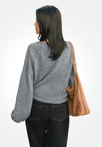 Suéter de punto gris con mangas abullonadas, patrón texturizado y dobladillo acanalado, combinado con jeans negros y un bolso de hombro de ante marrón.