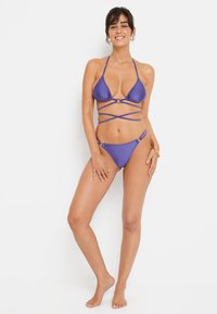 Set bikini viola con top a triangolo e lacci incrociati, arricchito da hardware circolare, completato da uno slip a vita bassa coordinato.