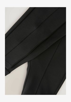 Mustad mustad on korralikult volditud, näidates oma siledat tekstuuri ja õmblusi heleda neutraalse tausta taustal.