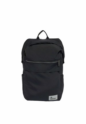 Mochila negra con un bolsillo frontal con cremallera, bolsillos laterales, asa superior y una pequeña etiqueta rectangular en la esquina inferior derecha.
