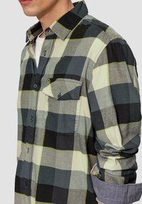 Zwart, grijs en groen geruite flanellen shirt met een knoopsluiting op de borst en opgerolde mouwen. Getextureerde stof, standaard kraagontwerp.