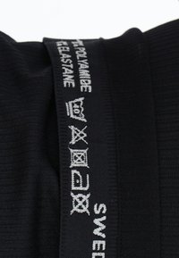 Sort tekstil med ribbet struktur, der har hvide broderede labels med plejemærker og teksten "SVERIGE". Stofsammensætningen inkluderer polyamid og elastan.